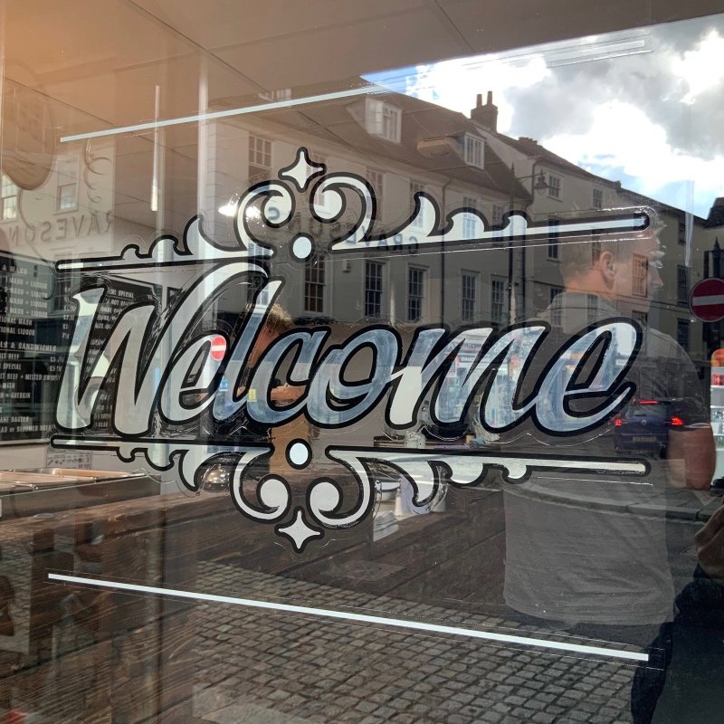 close up of Welcome sign hand painted by signwriter Joha Mune on the door of a shop in England